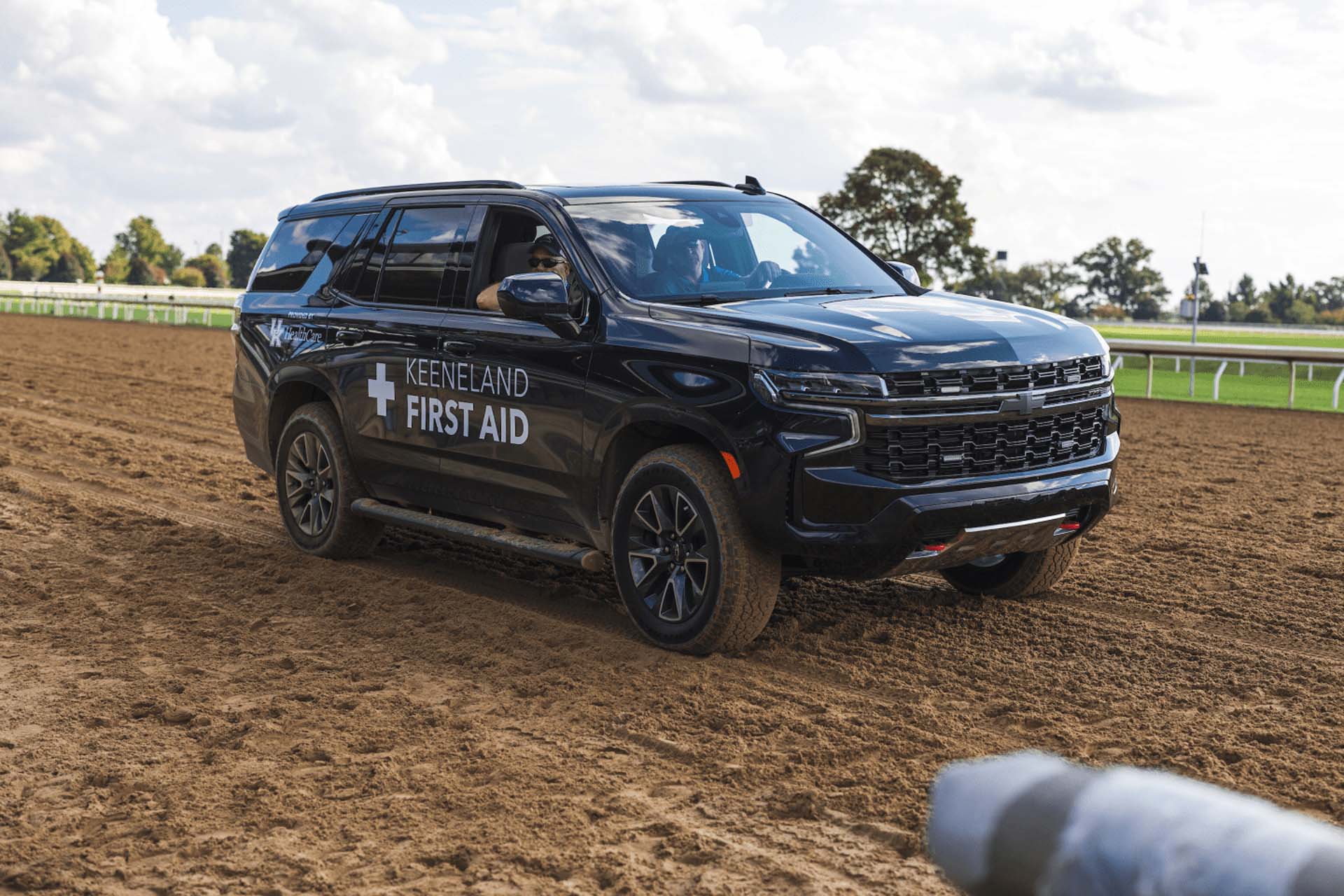 A picture of the Keenfieldview First Aid car on the dirt track. It is a large black Chevy SUV.